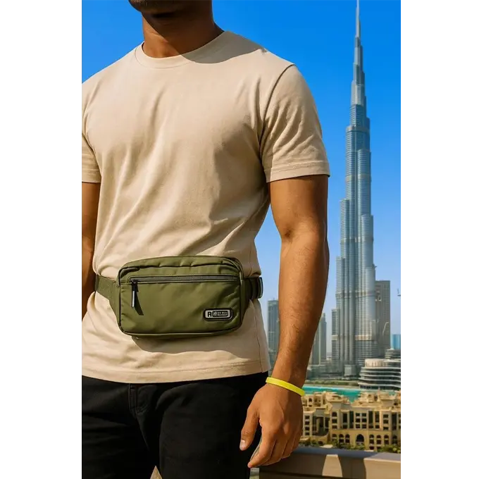 Sac banane vert kaki — porté en bandoulière croisée par un homme en t-shirt noir, vue urbaine floue en arrière-plan, badge Sport Clomert, fermetures éclair métalliques noires